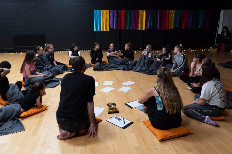Artist duo Webb-Ellis sit on the floor of a school drama studio in discussion with a group of 15 students.